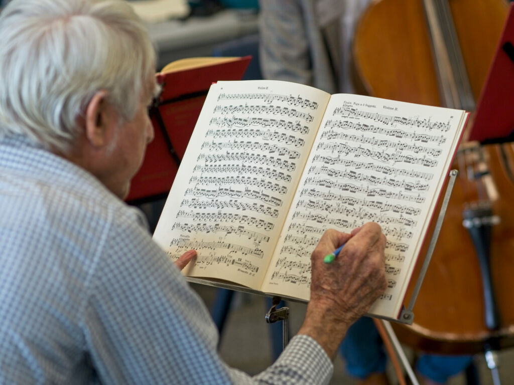 An elderly man writes on a music score.