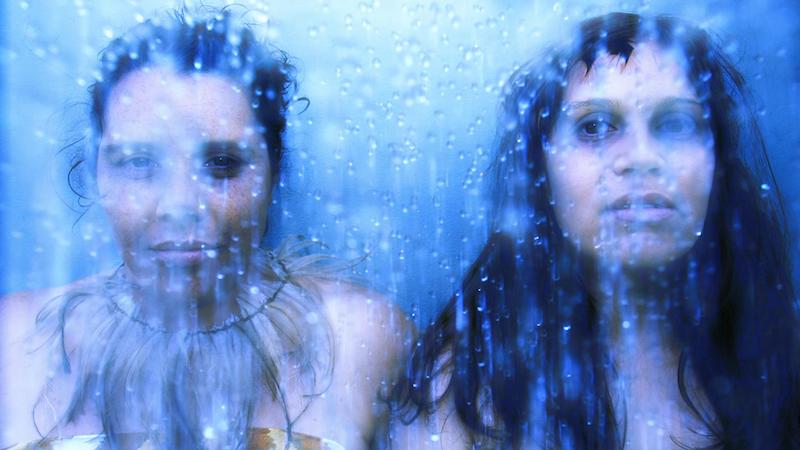 Two women stand behind a misty glass.