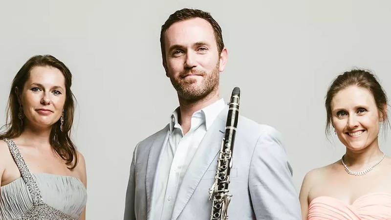 Two women smile, with a male clarinettist between them.