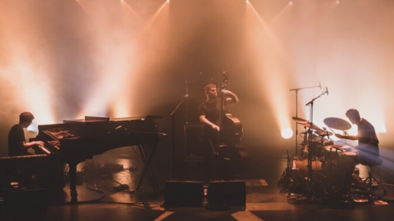 A pianist, double bassist and drummer make up GoGo Penguin and perform under warm lights on stage.