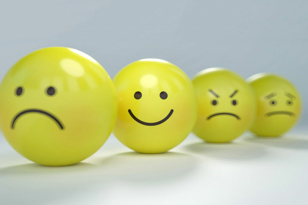A row of four yellow balls with faces on them ranging from sad, happy, angry and worried. The happy face is in focus, the others more blurry.