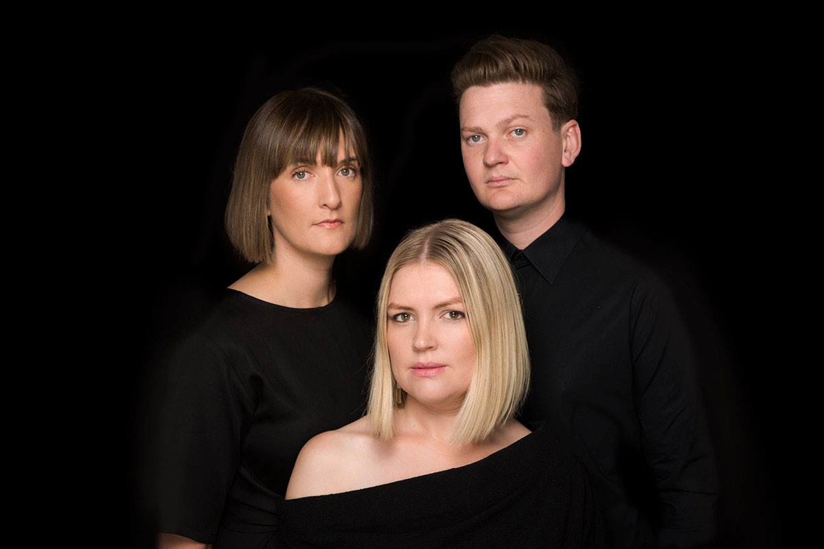 Louisa Rankin, Gian Slater and Josh Kyle in all -black against a black background, looking at the camera.