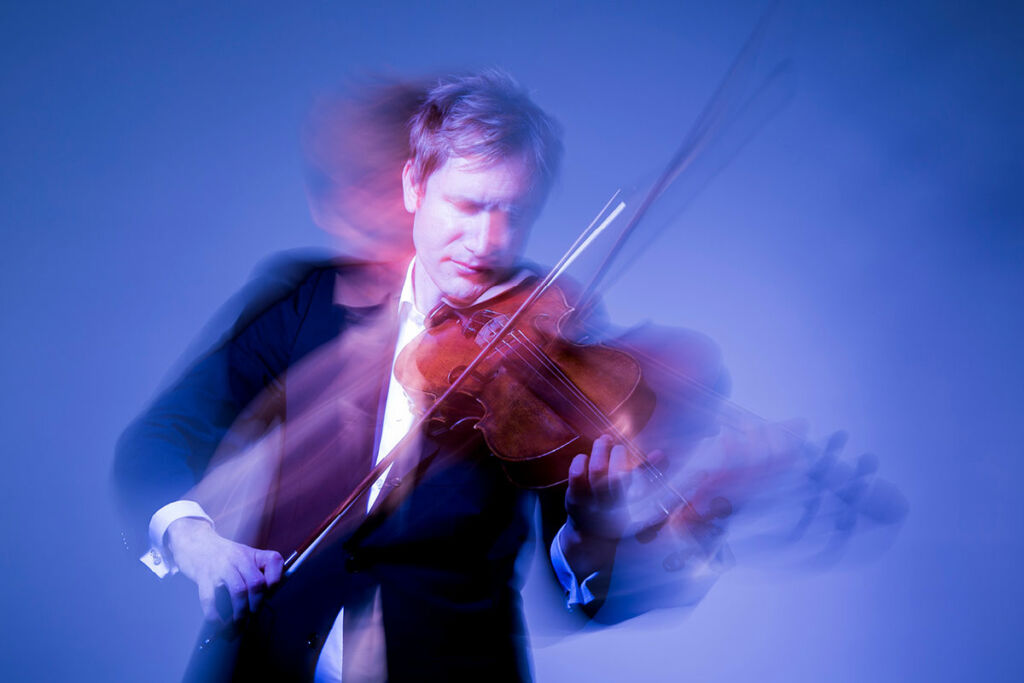 Justin Williams looks blurry in motion as he performs on his violin against a blue backdrop.