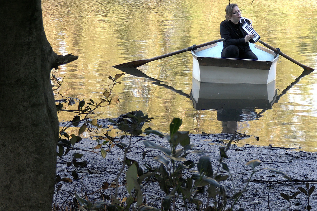 Elizabeth Jigalin plays the melodica in a rowboat in the Cooks River, just off its banks.