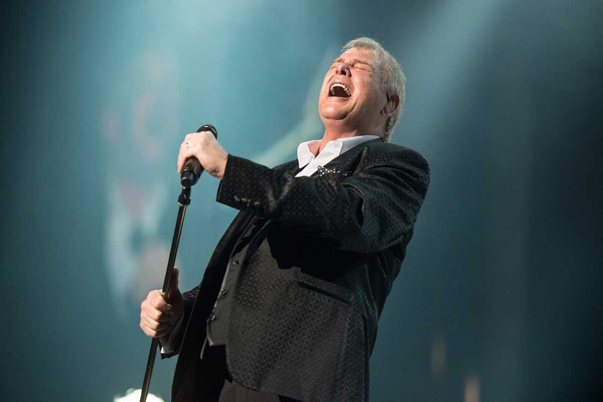 John Farnham belts into a microphone on stage.