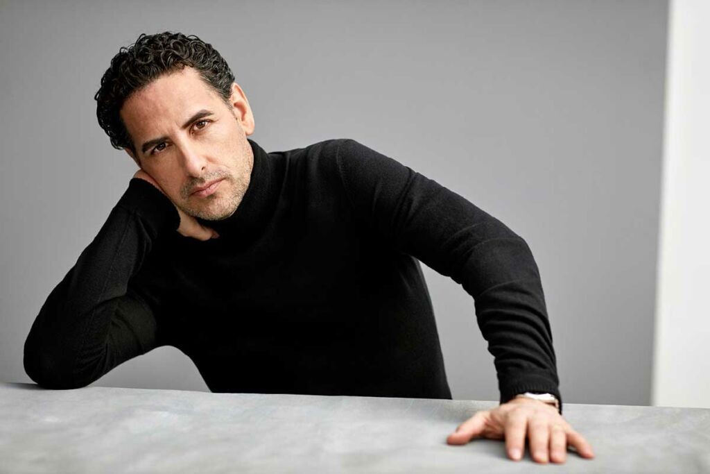 Juan Diego Flórez in a black turtleneck, seated at a table.