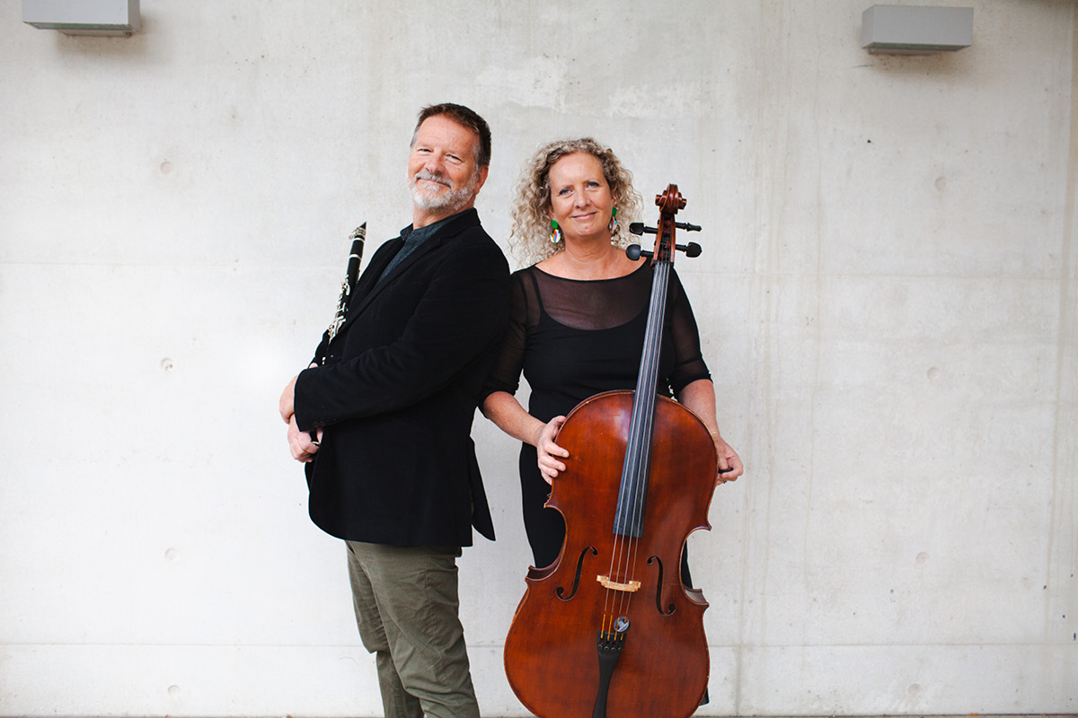 Paul Dean stands holding his clarinet with his back turned to Trish Dean, who faces forward holding her cello.