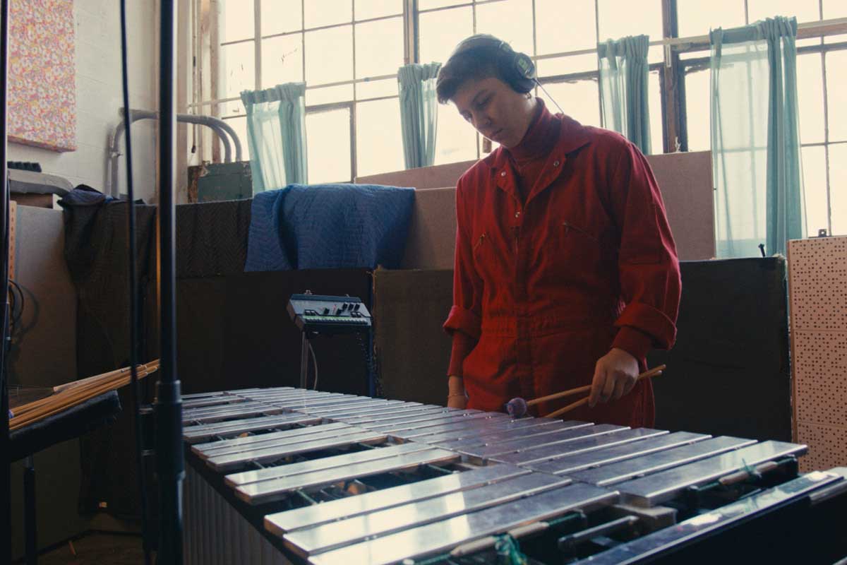 Sofia plays the vibraphone in a red jumpsuit in a shot from a short film work.