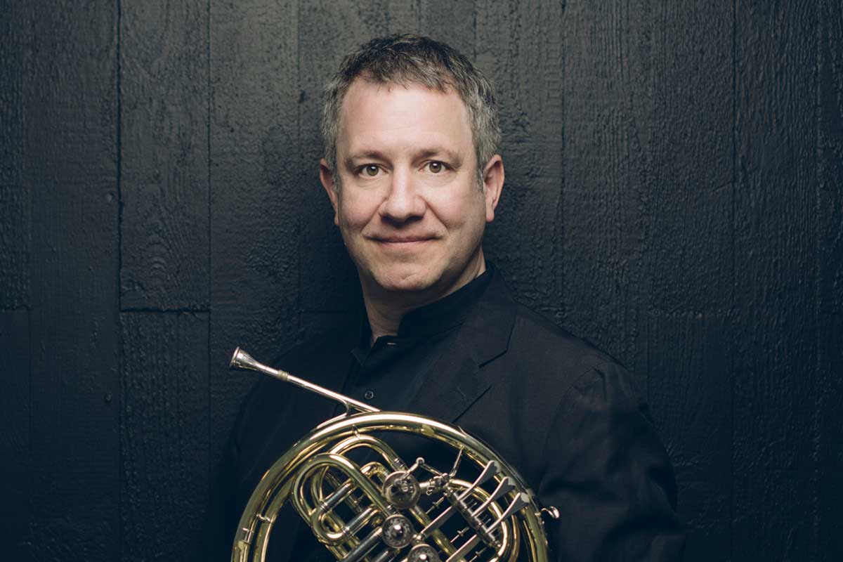 Stephan smiles, holding his French horn.