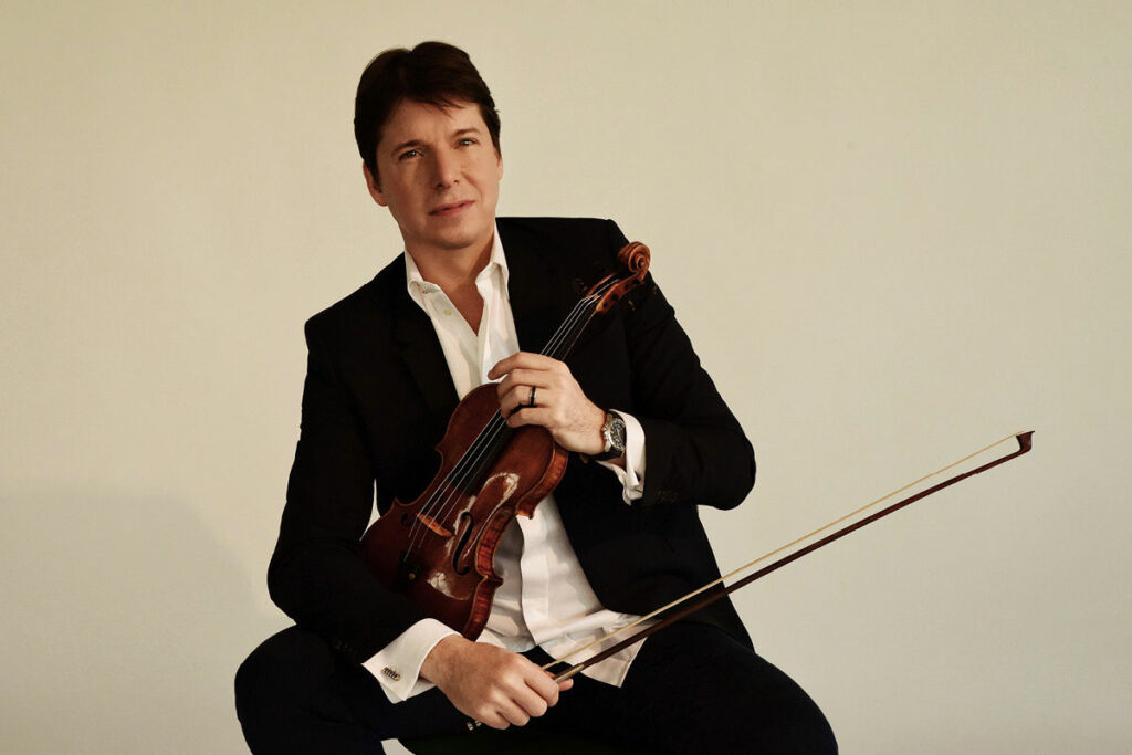 Joshua Bell holds his violin, sitting down.