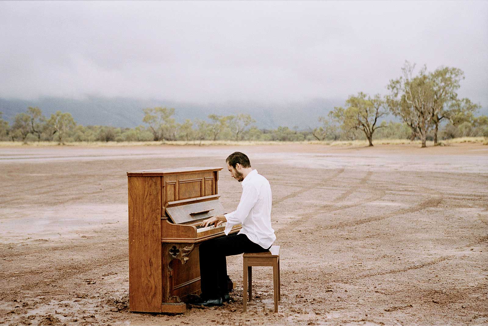 Dave Crowe plays a piani in the midst of a remote clearing in Central Australia.