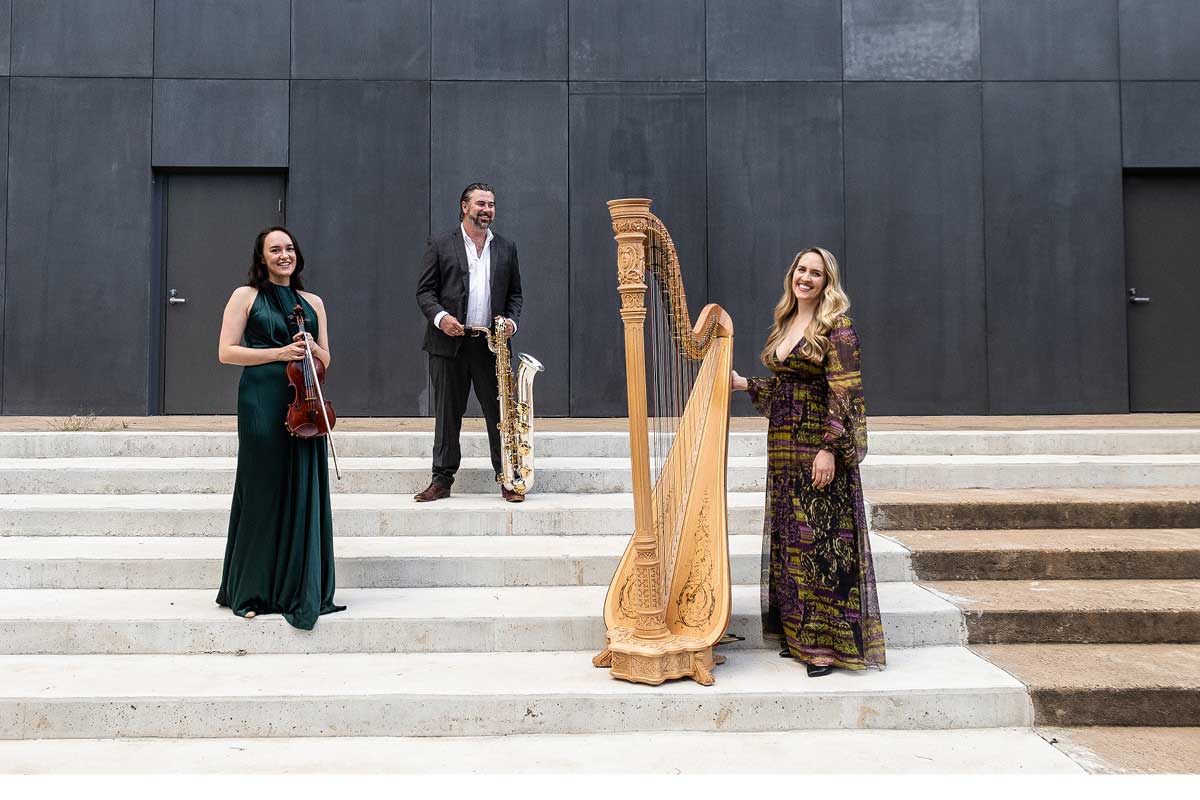 Orange Chamber Music Festival musicians Rachael Kwa, Jay Byrnes and Emily Granger stand on an outdoor staircase with their instruments.