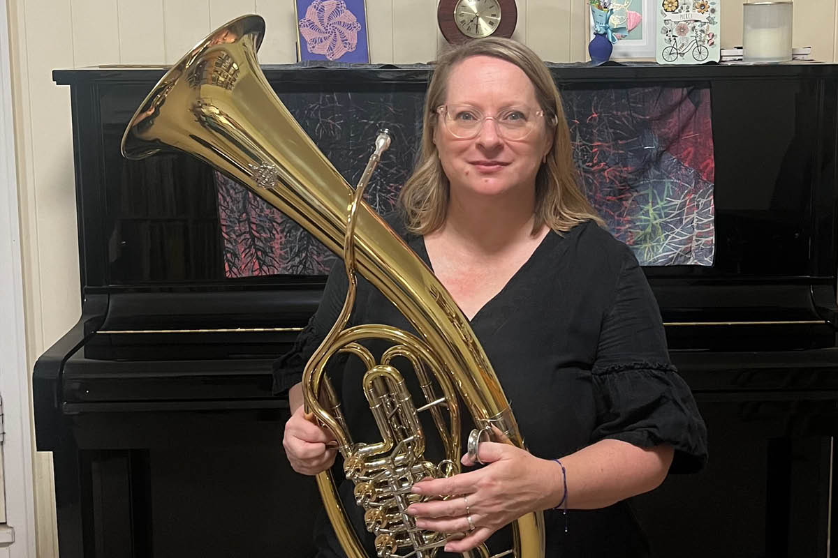 Ysolt Clark holding her Wagner tuba, sitting on a piano stool.