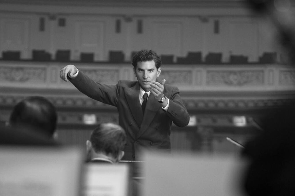 Bradley Cooper as Leonard Bernstein in the film Maestro, conducting an orchestra.
