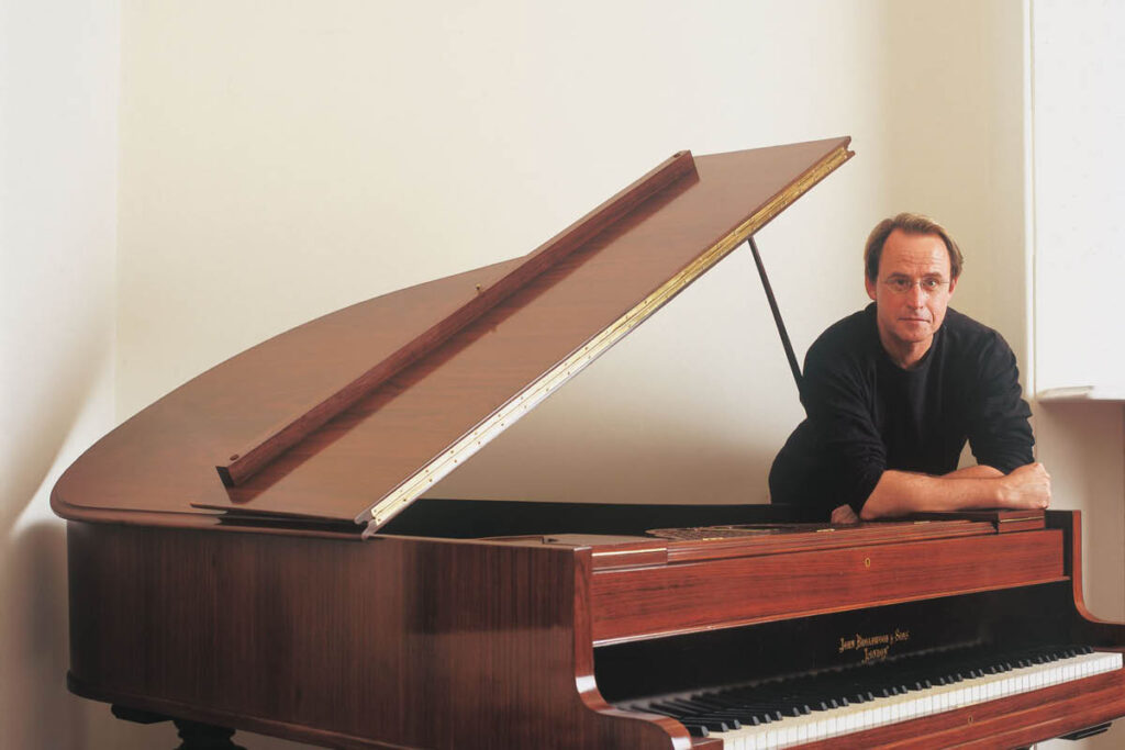 Graeme Koehne leans on a piano.