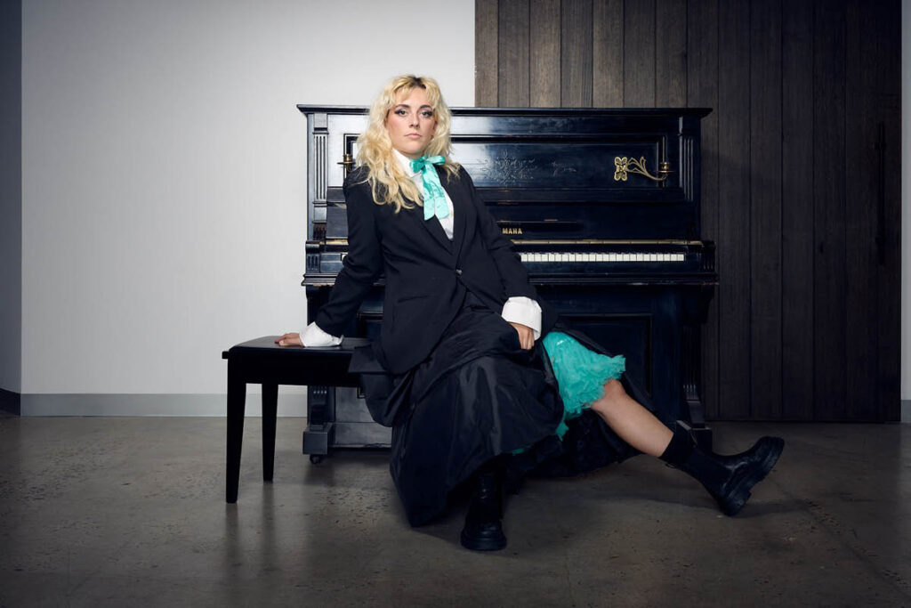Kala Gare in costume as Sybylla Melvyn, sitting by a piano, for Melbourne Theatre Company’s production of the new musical My Brilliant Career.
