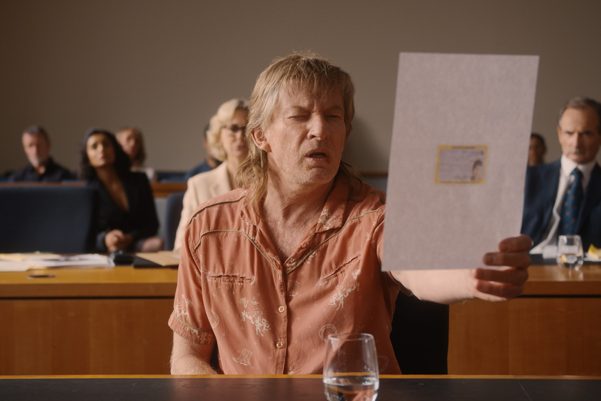 Spit (David Wenham) reading a document in court, squinting at it.