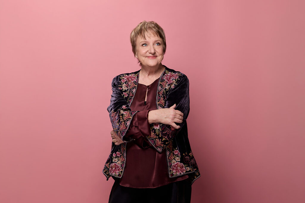 Denise Scott smiles, crossing her arms.